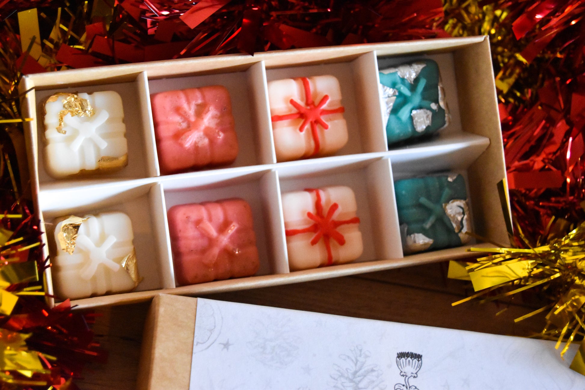 Box of assorted small wax melts with decorative packaging on a festive background